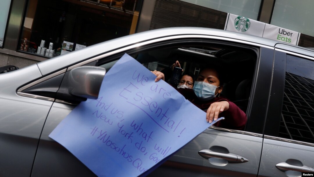 Seorang pekerga menunjukkan poster dalam unjuk rasa menuntut hak-hak pekerja imigran yang melakukan pekerjaan esensial di New York, di tengah pandemi virus corona (Covid-19) di New York, 21 April 2020. (Foto: Reuters)
