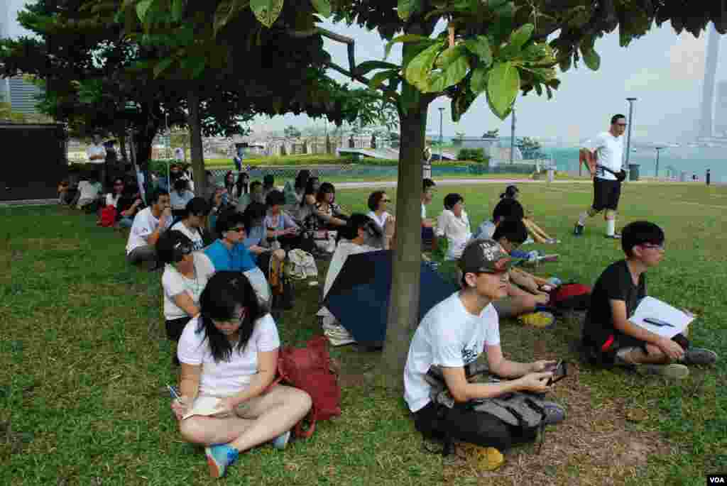 烈日當空下很多罷課學生躱在樹蔭下參與添馬公園的公民講堂