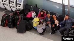Para penumpang duduk dekat koper mereka di dalam terminal JetBlue Airways di John F. Kennedy International Airport, New York. 