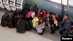 Travelers sit near their luggage inside the JetBlue Airways terminal at John F. Kennedy International Airport in New York, Jan. 6, 2014. 