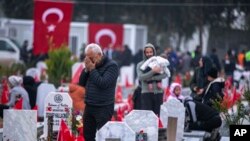 ARCHIVO - Personas visitan tumbas en un cementerio donde están enterradas algunas de las víctimas del terremoto de febrero de 2023 en Antakya, sur de Turquía, el martes 6 de febrero de 2024. AP