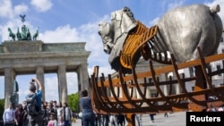 A man takes a picture near a piece of a traveling art exhibition called "Lapidarium, Waiting for the Barbarians" by Mexican artist Gustavo Aceves, in front of Brandenburg Gate in Berlin, Germany, May 4, 2015.