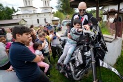 Children pose on motorcycles belonging to the members of the group Bikers for Humanity during an eyesight examination event, in Nucsoara, Romania, Saturday, May 29, 2021. (AP Photo/Vadim Ghirda)