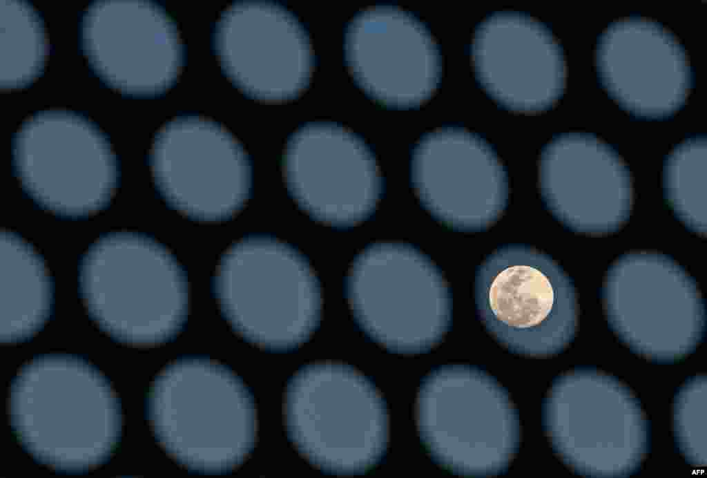 The full moon is seen behind a building&#39;s sun shade in Bangkok, Thailand.