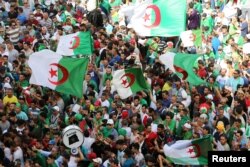 FILE - Demonstrators gesture and carry flags during a protest demanding the removal of the ruling elite and prosecution of former officials linked to former President Abdelaziz Bouteflika, in Algiers, Algeria, June 14, 2019.