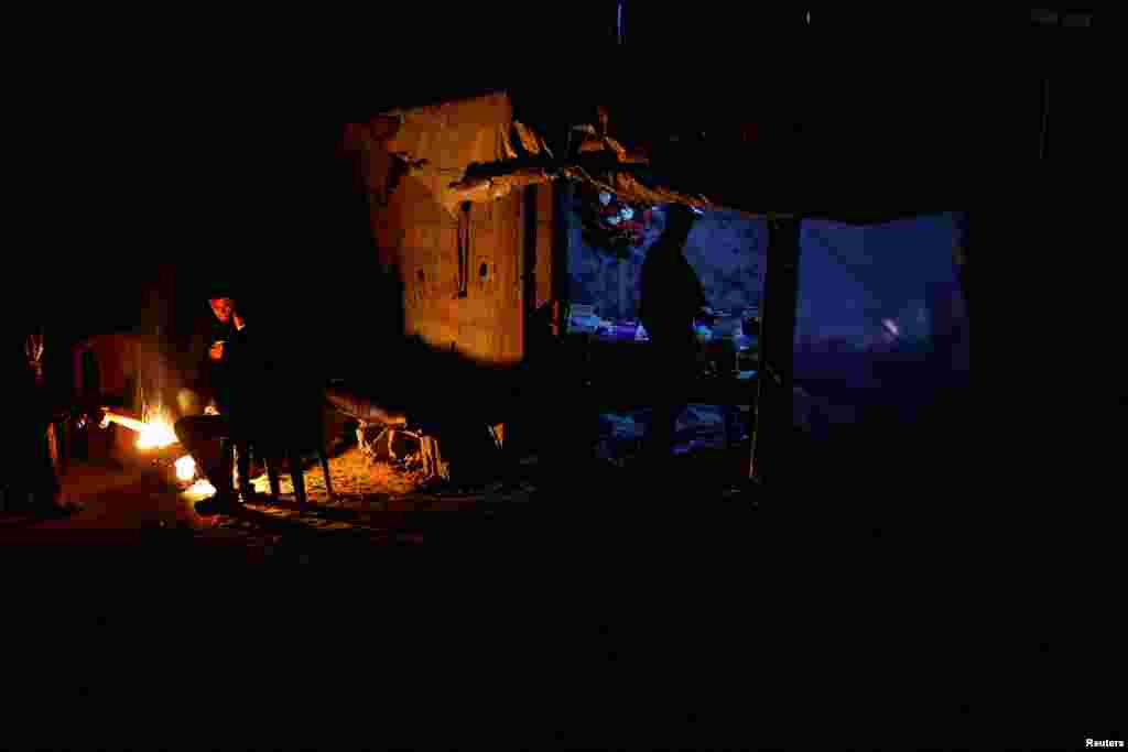 Palestinians sit around a fire as a man stands at a makeshift shop during a power cut in Rafah in the southern Gaza Strip, March 9, 2025.