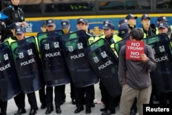 A protester against U.S. President Donald Trump covers his face with a placard while waiting for Trump's motorcade to pass by as police stand guard in central Seoul, Nov. 7, 2017.