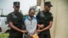 Callixte Nsabimana (C), porte-parole du groupe rebelle du Front de libération nationale (FLN), est escorté par des policiers au tribunal de première instance de Gasabo à Kigali le 23 mai 2019.