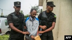 Callixte Nsabimana (C), porte-parole du groupe rebelle du Front de libération nationale (FLN), est escorté par des policiers au tribunal de première instance de Gasabo à Kigali le 23 mai 2019.