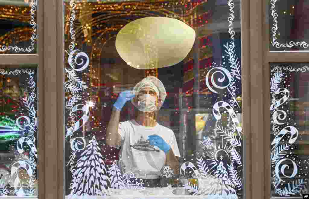 A cook in a face mask is seen making a pizza through a window glass decorated with Christmas ornaments in a city pizzeria in Kyiv, Ukraine.