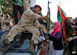 FILE - Libyan revolutionary fighter returning from Sirte is welcomed at Al Guwarsha gate in Benghazi, Libya, Oct. 22, 2011.