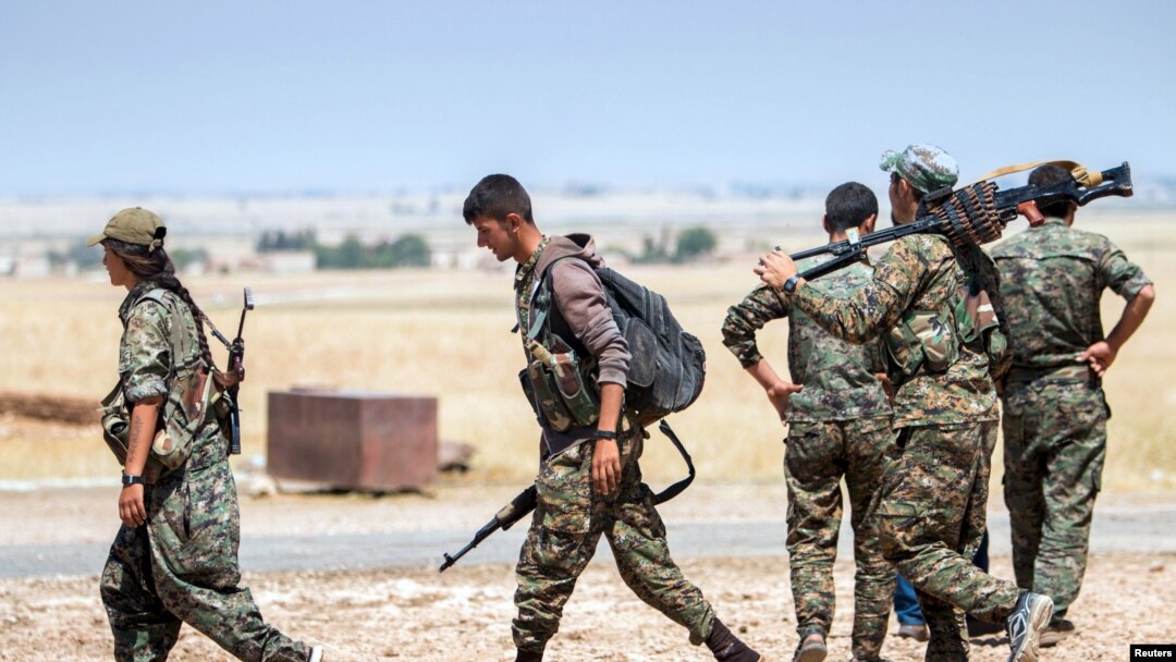 FILE- Kurdish fighters walk with their weapons outside the town of Tal Abyad, Syria, June 14, 2015.