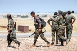 FILE- Kurdish fighters walk with their weapons outside the town of Tal Abyad, Syria, June 14, 2015.