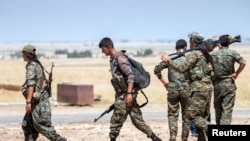 FILE- Kurdish fighters walk with their weapons outside the town of Tal Abyad, Syria, June 14, 2015.