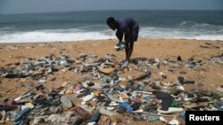 Ivorian painter Aristide Kouame 26, who paints optical effects artworks with worn soles, picks up used flip-flops among the garbage on a beach in Abidjan, Ivory Coast August 2, 2021. (REUTERS/Luc Gnago)