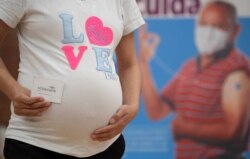 Seorang ibu hamil menunjukkan kartu vaksinasi setelah menerima dosis vaksin Pfizer-BioNTech melawan COVID-19 di pusat vaksinasi di Bogota, pada 23 Juli 2021 (Foto: AFP)