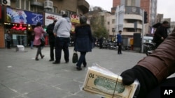 FILE - A street money exchanger holds Iranian and U.S. banknotes in downtown Tehran, Iran. 