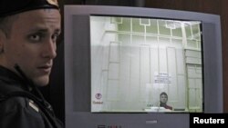 A bailiff stands next to a screen with a live broadcast of opposition activist Leonid Razvozzhayev's appeal at a Moscow court hearing, November 7, 2012.
