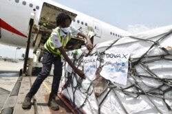 FILE - A woman attaches COVAX stickers to a shipment of AstraZeneca Covid-19 vaccine from a plane at Felix Houphouet Boigny airport of Abidjan on Feb. 26, 2021.