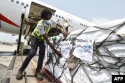 FILE - A woman attaches COVAX stickers to a shipment of AstraZeneca Covid-19 vaccine from a plane at Felix Houphouet Boigny airport of Abidjan on Feb. 26, 2021.