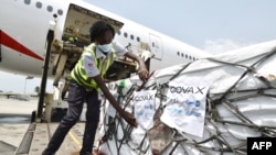 FILE - A woman attaches COVAX stickers to a shipment of AstraZeneca Covid-19 vaccine from a plane at Felix Houphouet Boigny airport of Abidjan on Feb. 26, 2021.