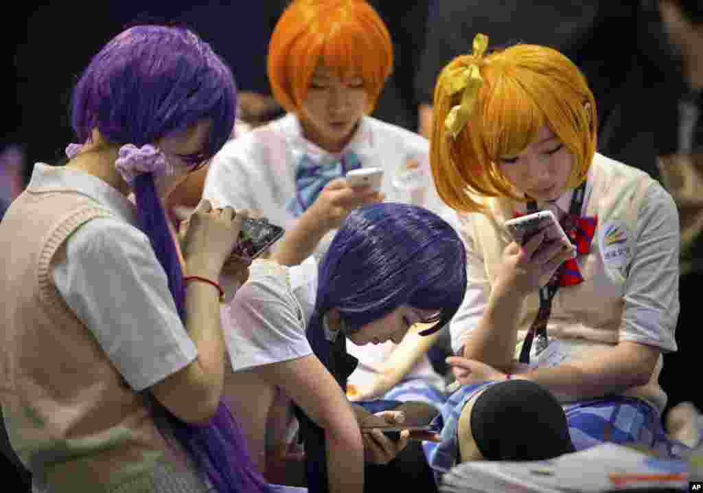 Models in costumes use their smartphones as they take a break at the Global Mobile Internet Conference in Beijing.