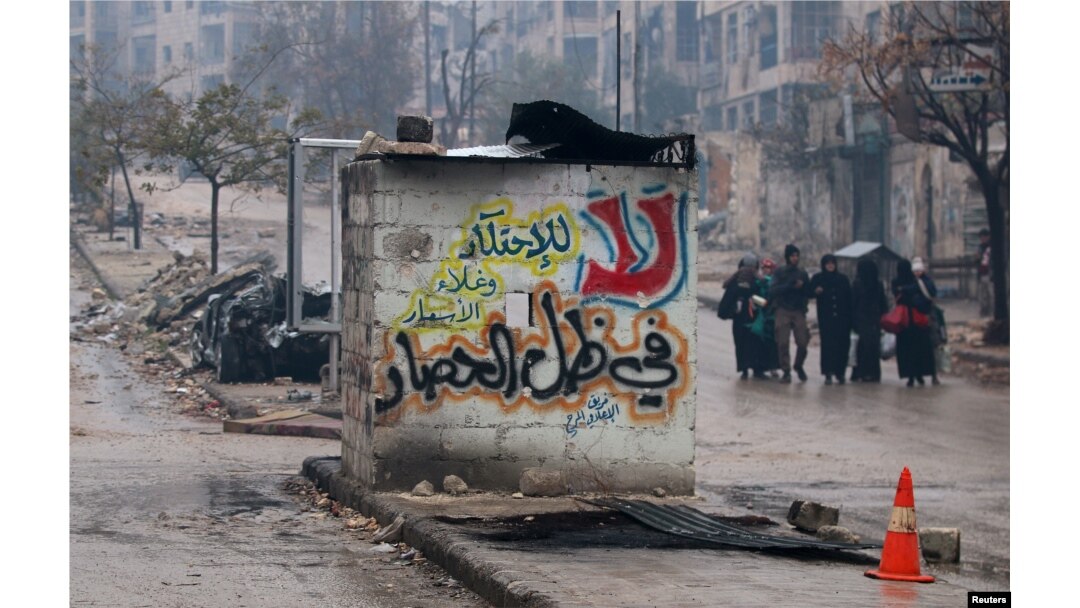 People carry their belongings as they flee deeper into the remaining rebel-held areas of Aleppo, Syria, Dec. 13, 2016. The Arabic words read, "No to monopolizing commodities and raising prices under the siege."