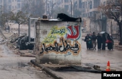 People carry their belongings as they flee deeper into the remaining rebel-held areas of Aleppo, Syria, Dec. 13, 2016. The Arabic words read, "No to monopolizing commodities and raising prices under the siege."