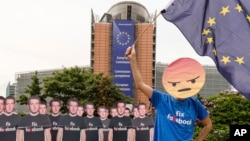 FILE - An Avaaz demonstrator waves the European flag as he stands next to life-sized Zuckerberg cutouts to protest against fake Facebook accounts spreading disinformation on the platform, near the EU Commission in Brussels, May 22, 2018.