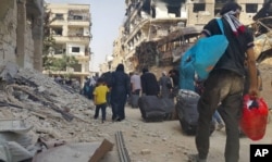 FILE - Syrian citizens carry their belonging as they prepare to evacuate from Daraya, a blockaded Damascus suburb, Aug. 26, 2016.