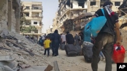 Syrian citizens carry their belonging as they prepare to evacuate from Daraya, a blockaded Damascus suburb, Friday, Aug. 26, 2016. The development in the Daraya suburb is part of an agreement struck between the rebels and government forces.