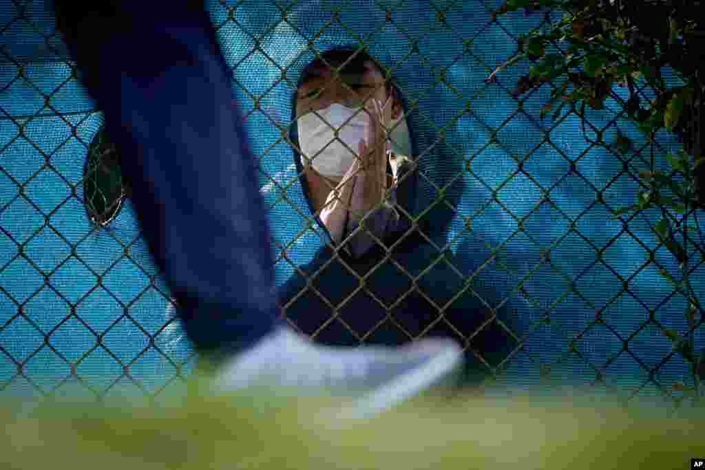 A fan wearing a face mask claps through a hole in the fence as a golfer leaves the 12th tee during the second round of the PGA Championship golf tournament at TPC Harding Park in San Francisco.