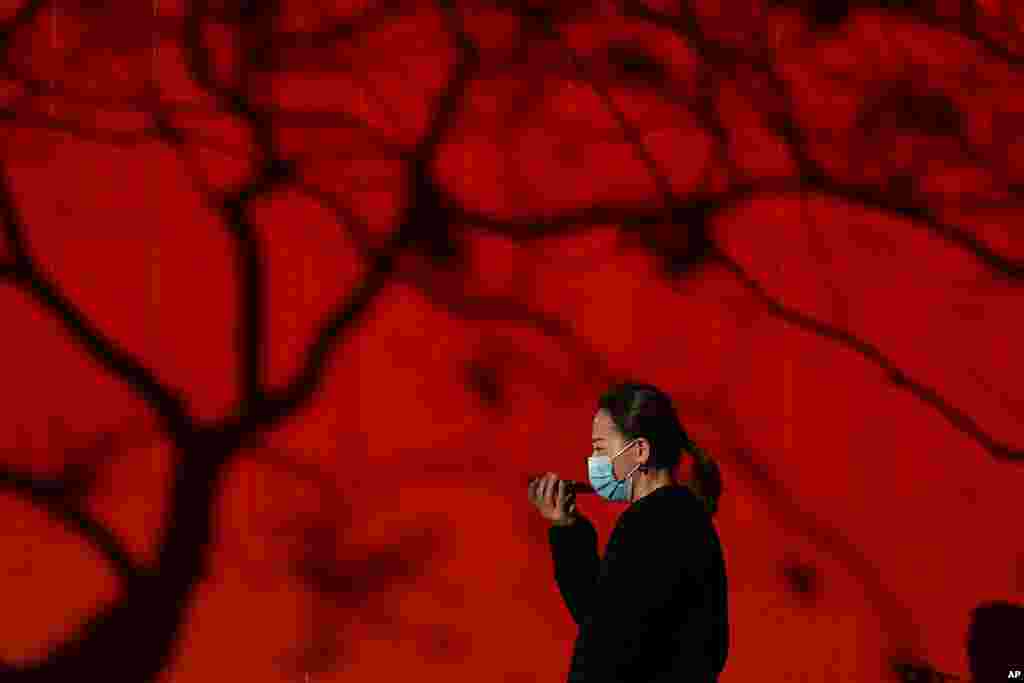 A woman wearing a face mask to help curb the spread of the coronavirus talks on her smartphone as she walks by tree shadow cast on a truck parked on a street in Beijing.