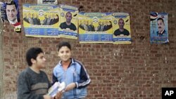 Boys stand near campaign posters of the Muslim Brotherhood's Freedom and Justice Party outside a polling station during the second day of parliamentary elections in the village of Kafr el-Moseilha, the hometown of former president Hosni Mubarak, December 