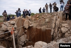 Orang-orang menyaksikan bagian luar terowongan tambang di Stilfontein, Afrika Selatan, tempat ratusan penambang ilegal diperkirakan bersembunyi di bawah tanah, setelah polisi menghentikan pasokan makanan dan air, 15 November 2024. (Ihsaan Haffejee/REUTERS)