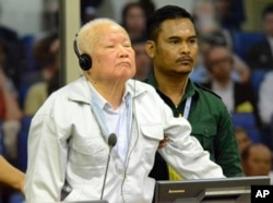 In this photo released by the Extraordinary Chambers in the Courts of Cambodia, Khieu Samphan, left, former Khmer Rouge head of state, stands at the dock in a courtroom during a hearing at the U.N.-backed war crimes tribunal in Phnom Penh, Cambodia, Nov. 16, 2018.