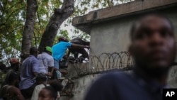 FILE - Journalists climb up a wall to take cover from gunfire, after being shot at by armed gangs at the General Hospital in Port-au-Prince, Haiti, Dec. 24, 2024.