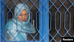 An Afghan inmate watches from behind a barred window during a media event at a women's prison in Kabul, March 30, 2010. 