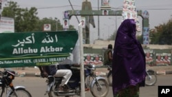 FILE- In this April 15, 2011, file photo, a Muslim woman walks past an Arabic sign on a street which reads 'God is great' in Katsina, Nigeria.