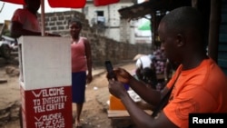 FILE - A man inspects a mobile phone at a 'telecenter' kiosk in Sierra Leone's capital, Freetown.