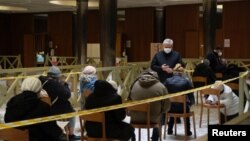 FILE - Cardinal Konrad Krajewski, the Polish head of the papal charities office, stands next to homeless people who are looked after in structures run by his office as they wait to receive their first dose of the vaccine against the coronavirus disease at