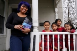 Dinora Torres, a MassBay Community College student, poses with her four daughters on the front porch of their home, Thursday, Jan. 14, 2021, in Milford, Mass. At the college, applications for meal assistance scholarships have increased 80% since last year