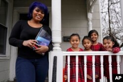 Dinora Torres, a MassBay Community College student, poses with her four daughters on the front porch of their home, Thursday, Jan. 14, 2021, in Milford, Mass. At the college, applications for meal assistance scholarships have increased 80% since last year