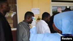 A health worker takes the temperature of people at a news conference on the opening of a new Ebola clinic, outside Monrovia, Oct. 3, 2014. 