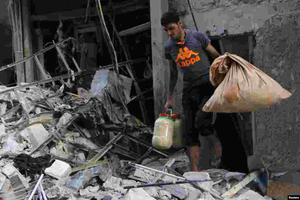 A man carries his belongings as he walks among debris from a collapsed buildings hit by what activists said was a barrel bomb dropped by forces loyal to President Bashar al-Assad, Bustan al-Qasr, Aleppo, May 28, 2014.