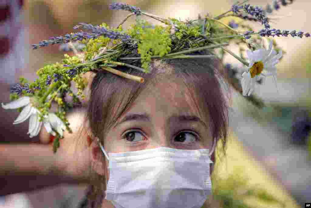 A girl wearing a face mask to combat the spread of the COVID-19 infections and a flower crown she made herself at a workshop stands during an event inspired by pre-Christian traditions at the Dimitrie Gusti Village Museum in Bucharest, Romania.