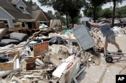 FILE - Volunteer Paul Hancock pushes an oven damaged by floodwaters onto a pile of debris in the aftermath of Hurricane Harvey on Sunday, Sept. 3, 2017, in Spring, Texas.