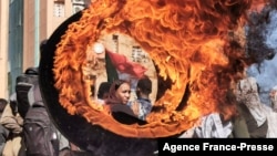 A demonstrator looks on from behind a flaming tire during a protest demanding civilian rule in the "Street 40" of the Sudanese capital's twin city of Omdurman, Jan. 4, 2022.