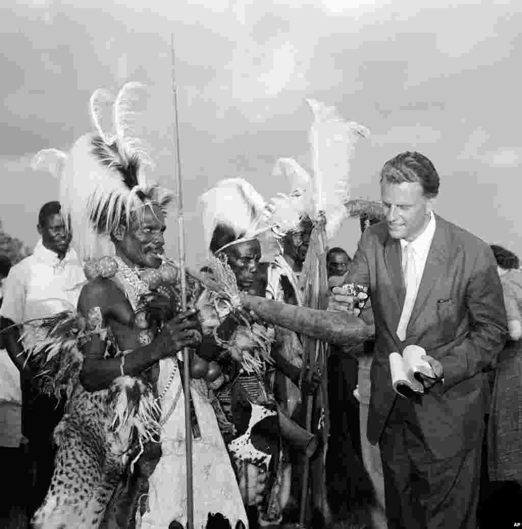 Le révérend Billy Graham examine la pipe d'un membre de la tribu de Joluo à Kisumu, au Kenya, le 6 mars 1960, lors de sa tournée en Afrique.