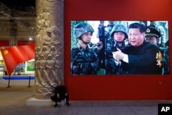 FILE - A man rests next a video screen showing Chinese President Xi Jinping holding a rifle at an exhibition highlighting China’s achievements under five years of his leadership at the Beijing Exhibition Hall in the capital city, Oct. 23, 2017.
